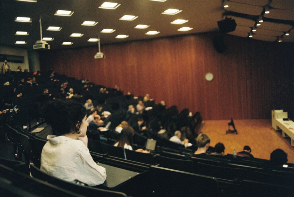 Students in a lecture auditorium viewing a presentation with live captioning displayed on a screen