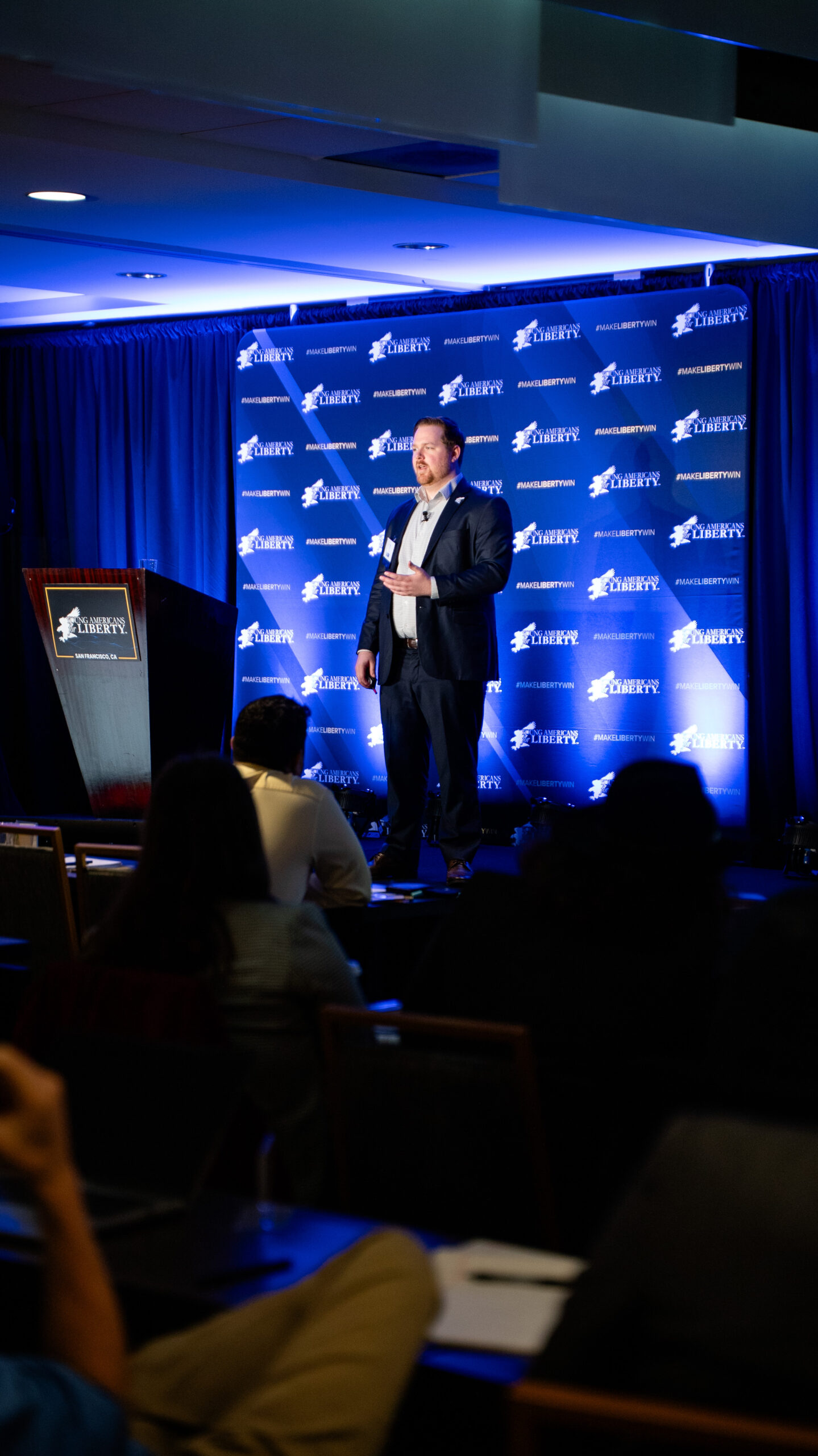 A speaker at the podium in front of a Young Americans for Liberty backdrop at YALCON: On Tour, with the audience in the foreground