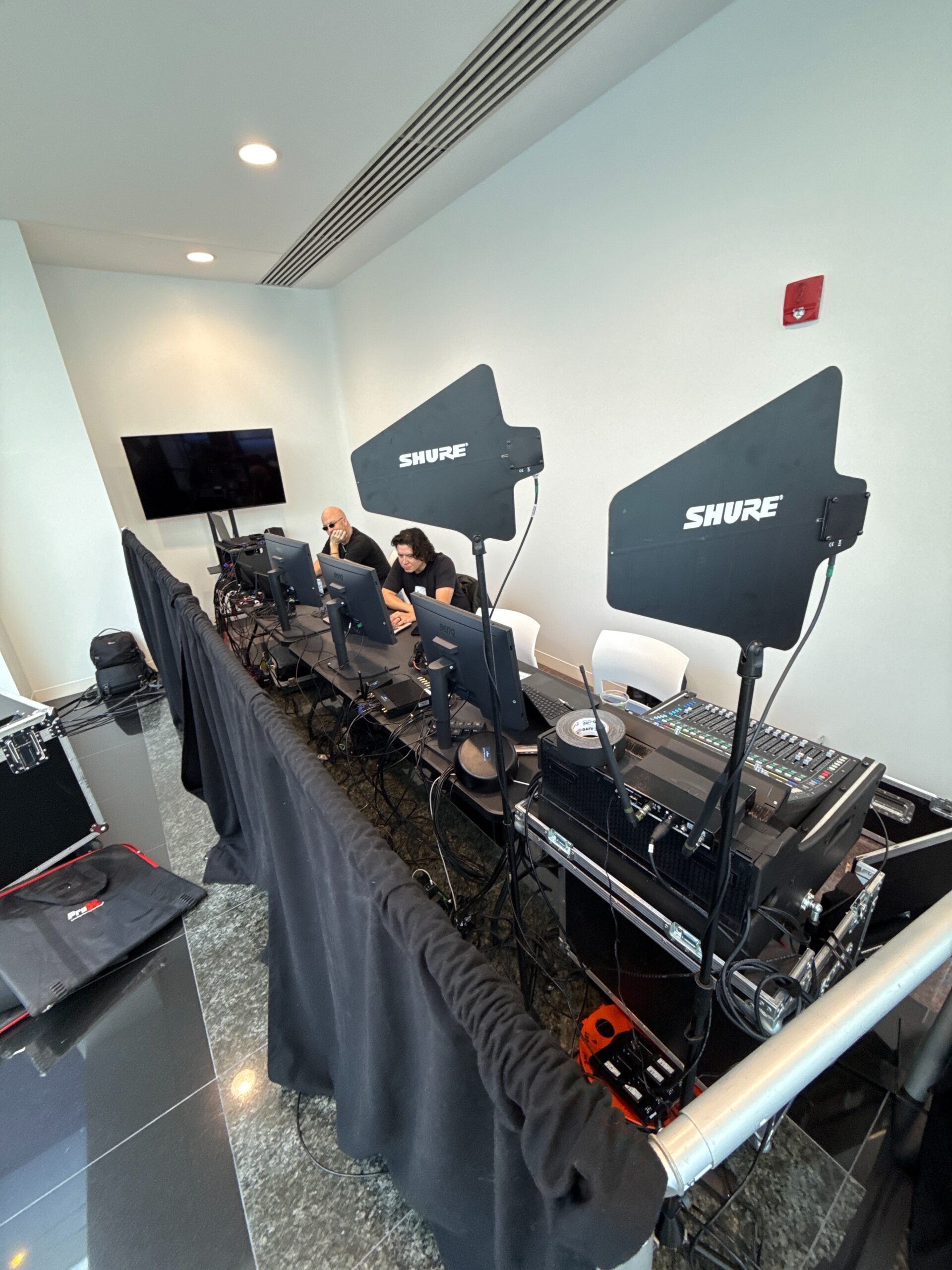 Front of house at a hybrid event: a mixing desk, monitors and two Shure wireless antenna paddles
