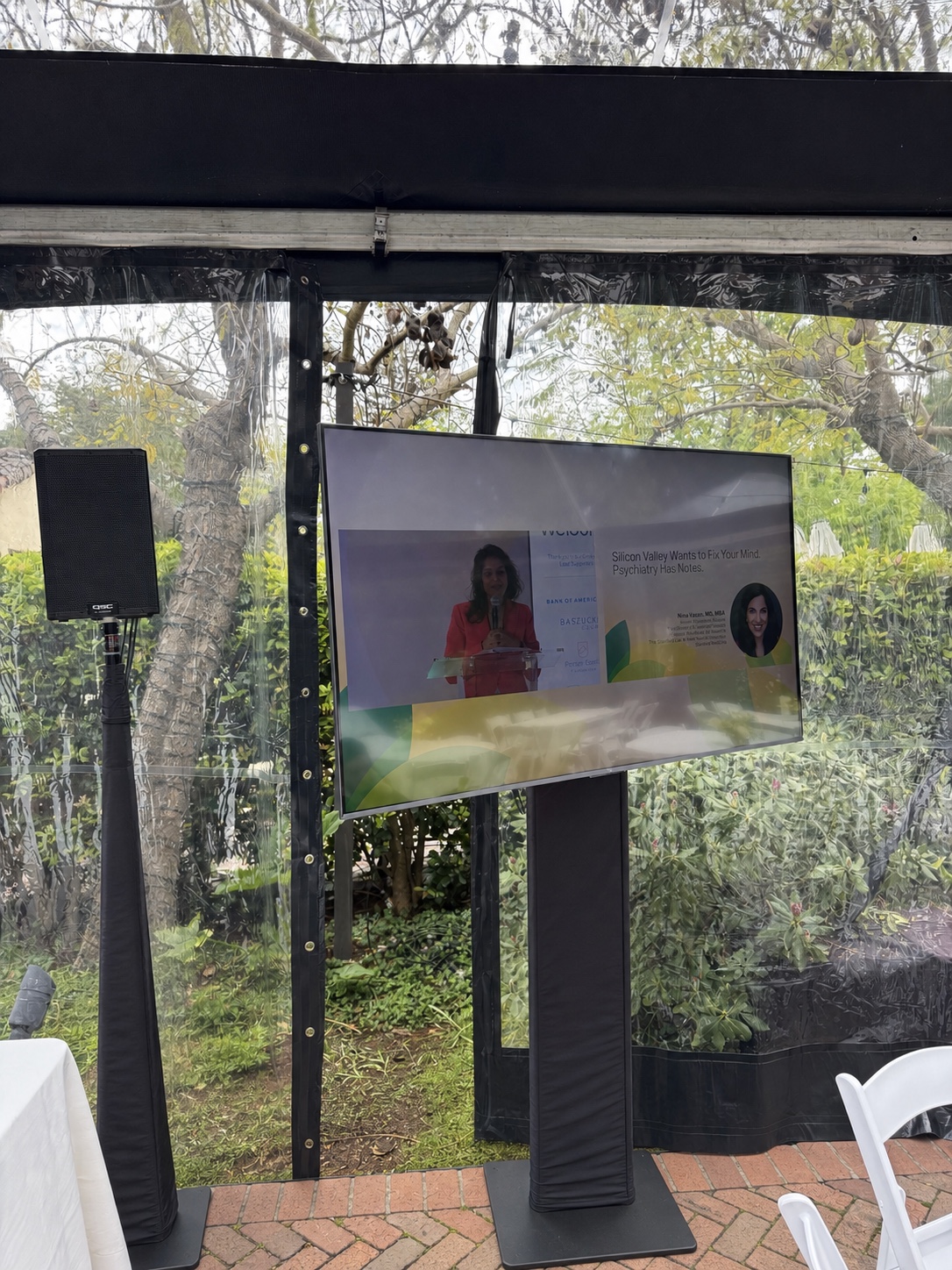 Outside tent at Allied Arts Guild with a 65 inch screen and speaker on stands carrying the live camera feed from the main session