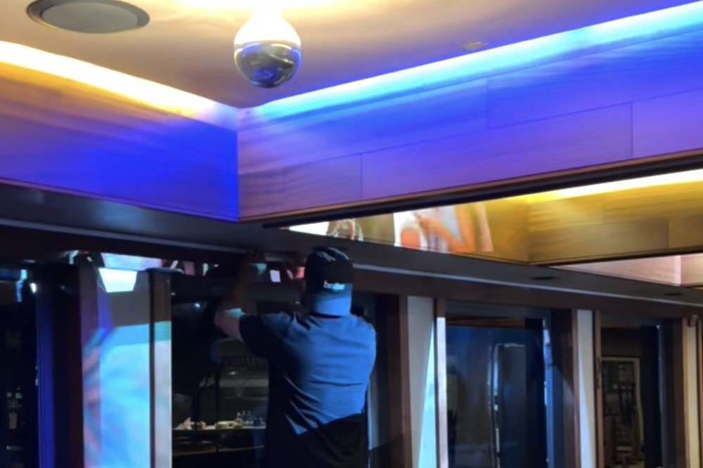 A technician installing cove lighting during the build at 1300 Battery Street, with projection running on the wall behind