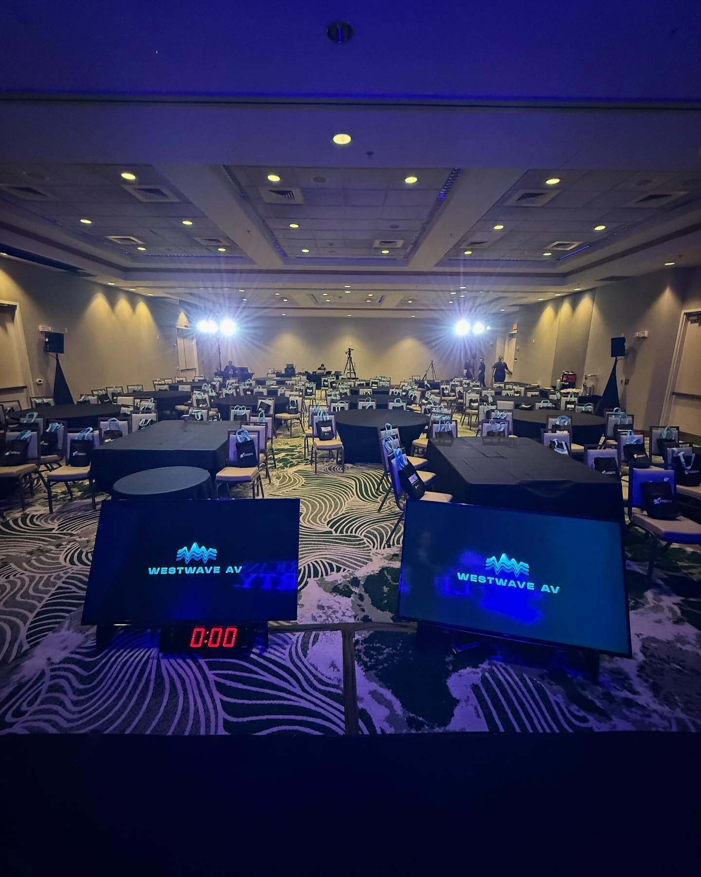 The same ballroom from the back, with confidence monitors on the tables and blue uplighting on the walls