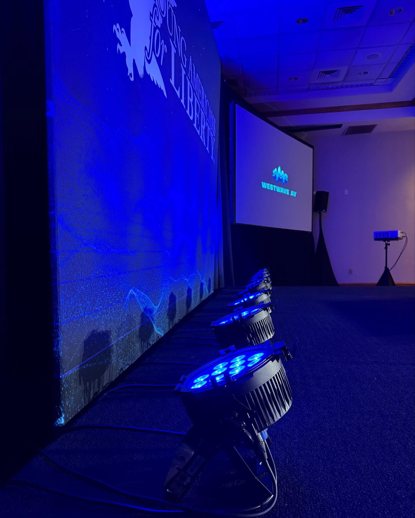A projected graphic across the stage wall in blue, with LED par cans in the foreground